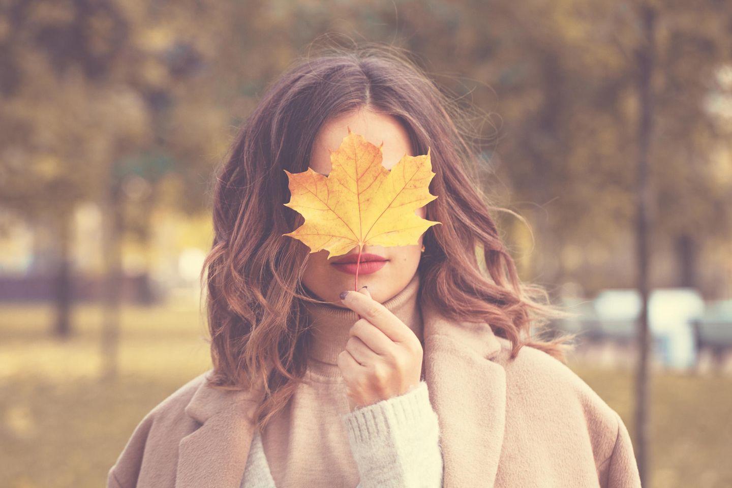 Das sagt Ihre liebste Jahreszeit über Ihren Charakter aus: Frau im Herbst mit Laub vor dem Gesicht.