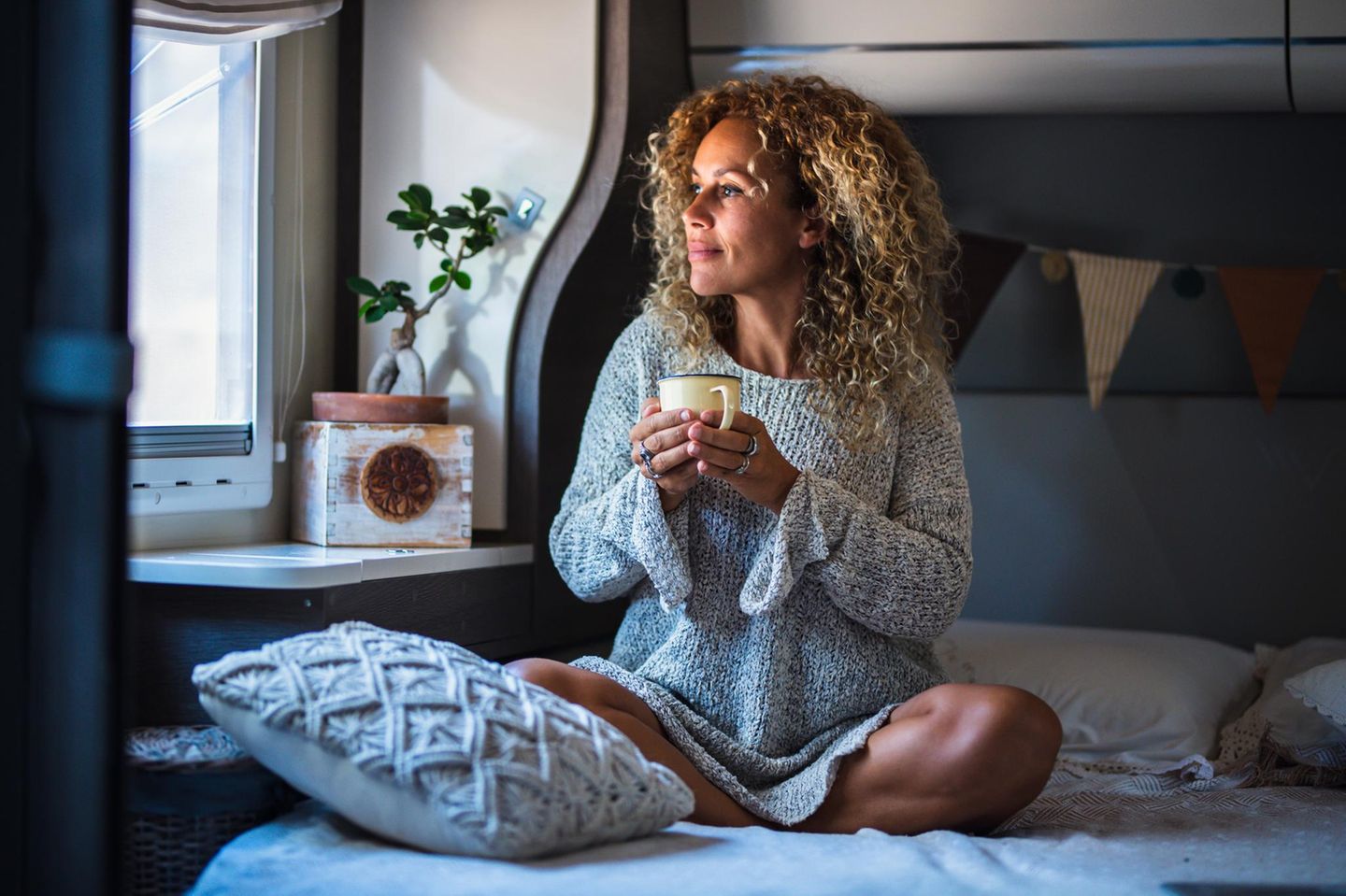 Gesund und Glücklich: Frau sitzt zufrieden und entspannt mit einem Tee in der Hand auf dem Bett