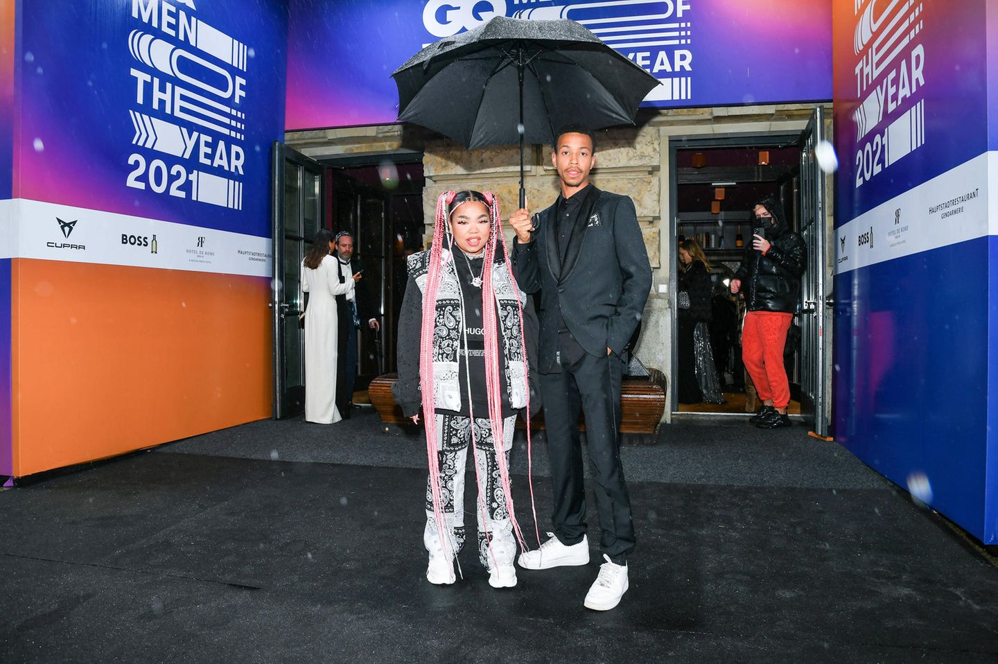 "Newcomer of the Year" Zoe Wees lässt sich ihren sportlichen Look und besonders die bodenlangen Braids in Pink von ihrem Freund Sulay vor dem Regen schützen.