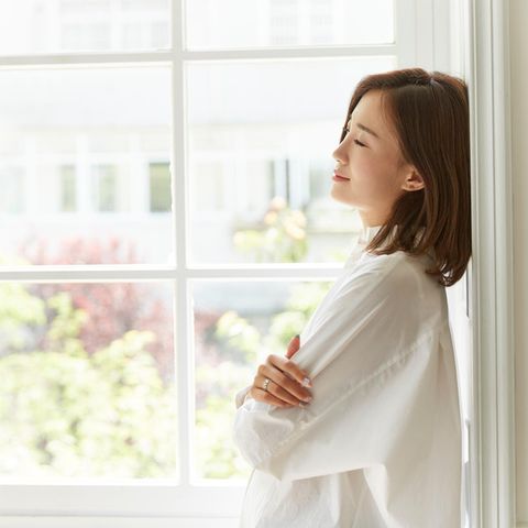 Frau entspannt am Fenster: Macht ein minimalistisches Leben glücklicher?