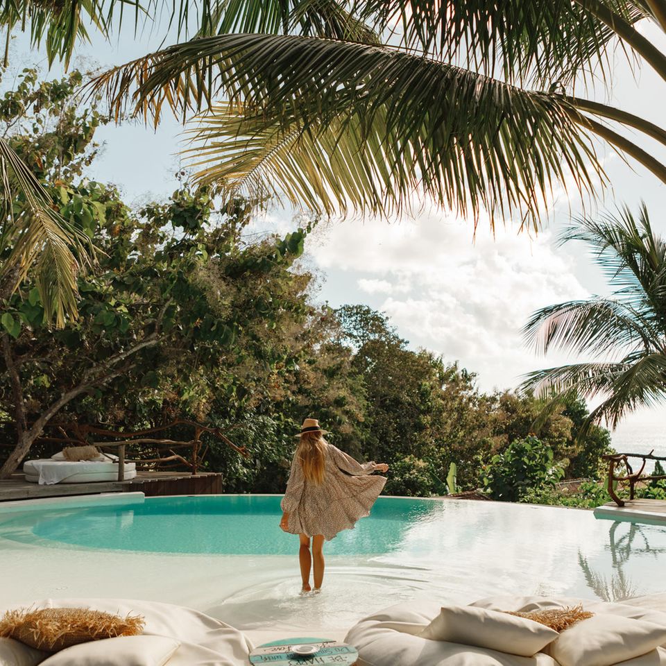 Frau am Pool zwischen Palmen: Das verraten Ihre Urlaubsvorlieben über Sie