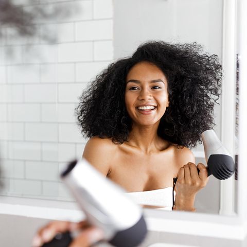 Lächelnde Frau in Handtuch bekleidet mit Föhn vor einem Spiegel