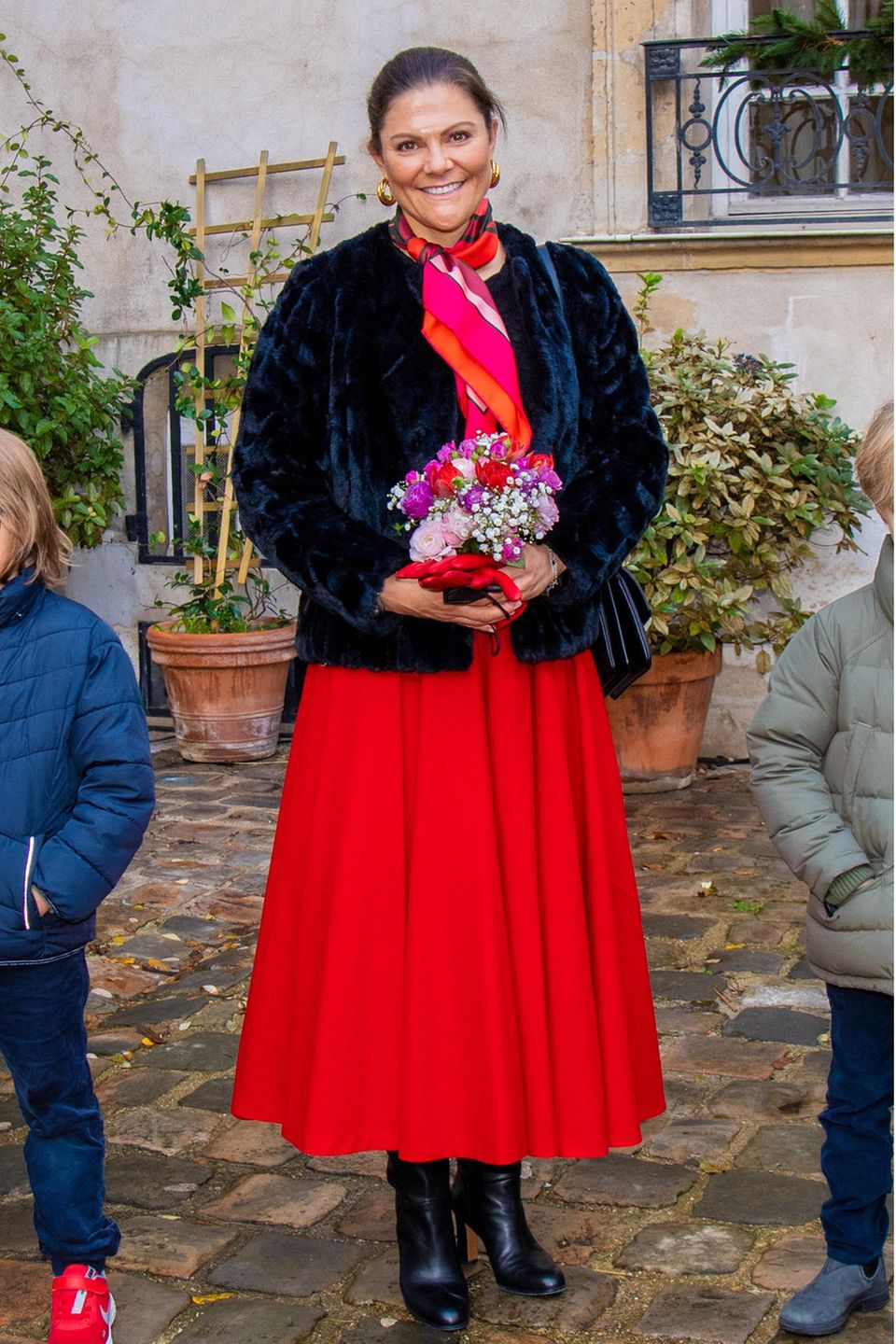 Bei ihrem Besuch in Paris setzt Prinzessin Victoria auf einen sehr klassischen Look, den man oft von ihr sieht: Sie trägt ein schwarzes Woll-Shirt, einen roten Midi-Rock und ein farblich passendes Halstuch. Besonders ist dagegen die dunkle Fake-Fur-Jacke, die ihr Outfit definitiv spannender macht. 