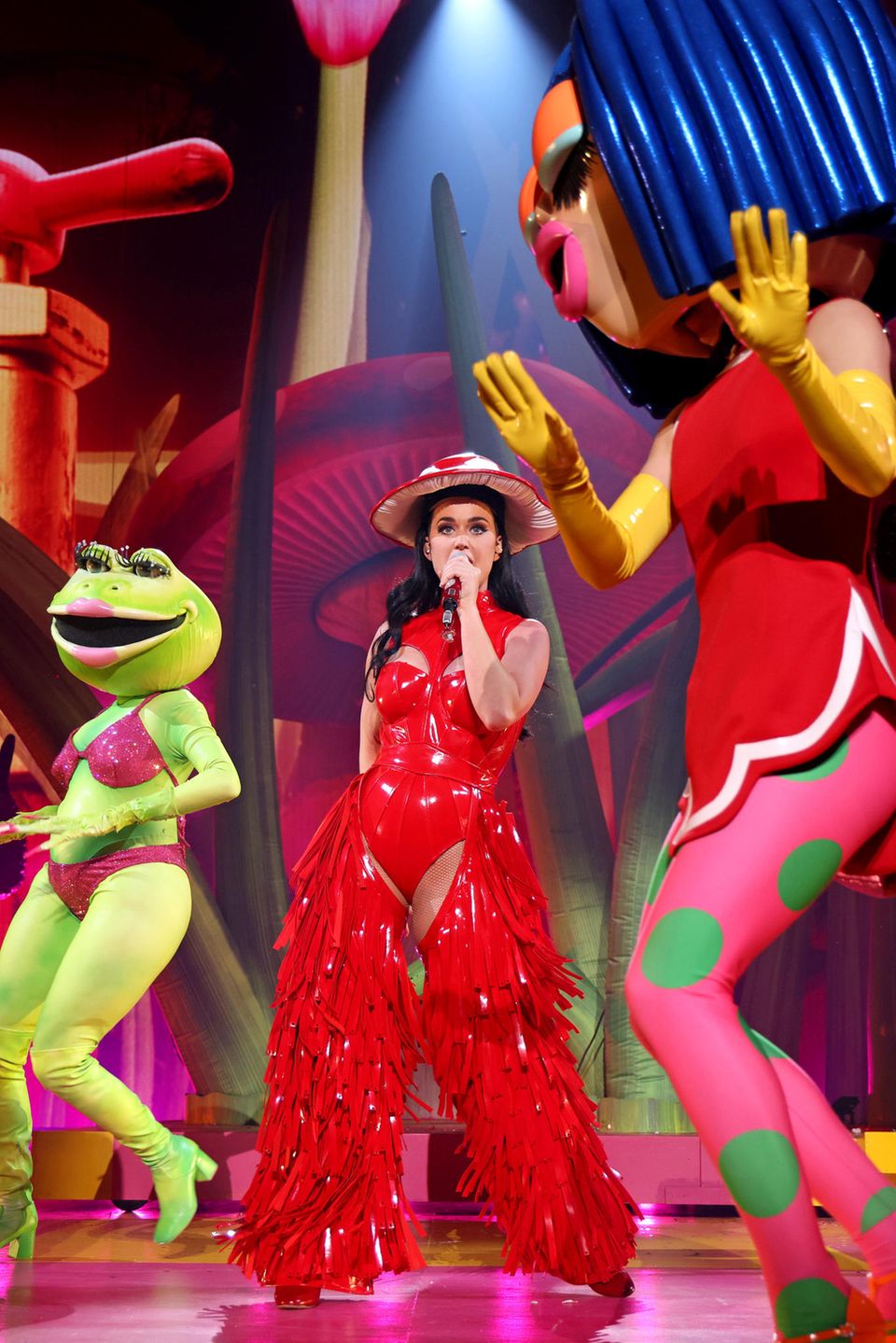Skurril und trotzdem elegant performt Katy Perry bei ihrer "PLAY"-Show in Las Vegas im Resorts World Theatre. Das Konzert ist mit einem aufwendigen Bühnenbild ausgestattet. Neben Fliegenpilzen, riesigen Masken und Trinkdosen fallen aber vor allem die Looks der Sängerin auf. Der rote Lack-Body mit Cut-Outs allein ist schon ein besonderes Kleidungsstück, aber in Kombination mit den roten fransigen Lack-Chaps ist dieser Look wirklich ein Hingucker. Der Fliegenpilz-Hut rundet das Outfit ab und zeigt, wie abgestimmt die Sängerin mit ihrem Bühnenbild ist. Auch die anderen Looks harmonieren perfekt mit den Requisiten.
