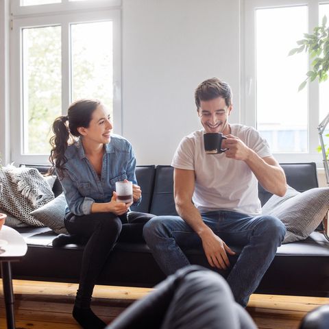 Eine Frau und ein Mann sitzen auf einem Sofa und trinken Kaffee.