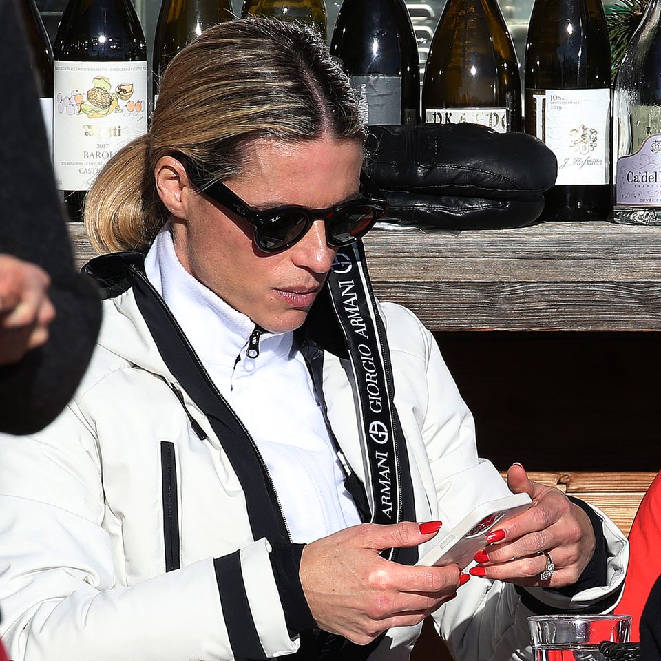 Michelle Hunziker sitzt im Ski-Outfit und Sonnenbrille an einem Tisch und schaut auf ihr Handy