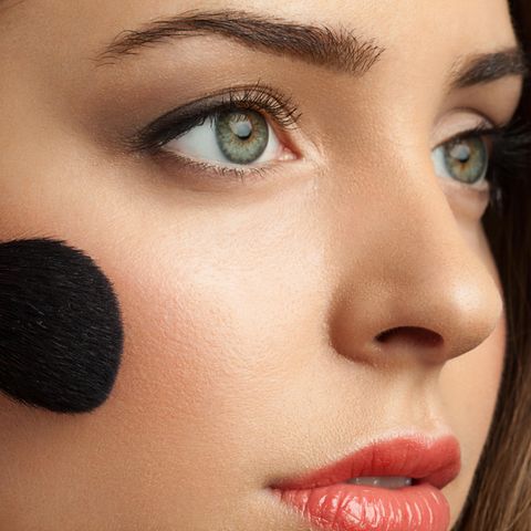 Rouge auftragen: Frau mit grünen Augen mit Make-up-Pinsel an Wangenknochen