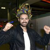 Menderes Bagci trägt eine Blumen-Krone auf dem Kopf und streckt freudig seine Hände nach oben.