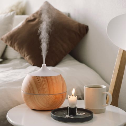 Aroma-Diffuser auf einem weißen Nachttisch, daneben eine Kerze und eine Tasse