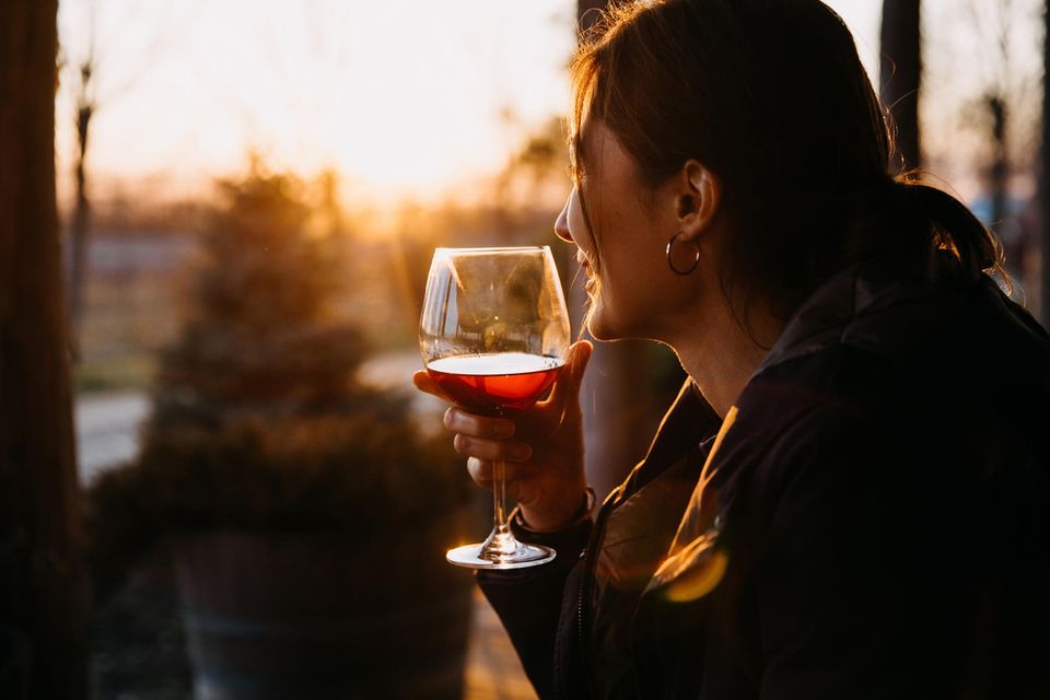 Eine Frau trinkt ein Glas Rotwein, während draußen die Sonne untergeht.