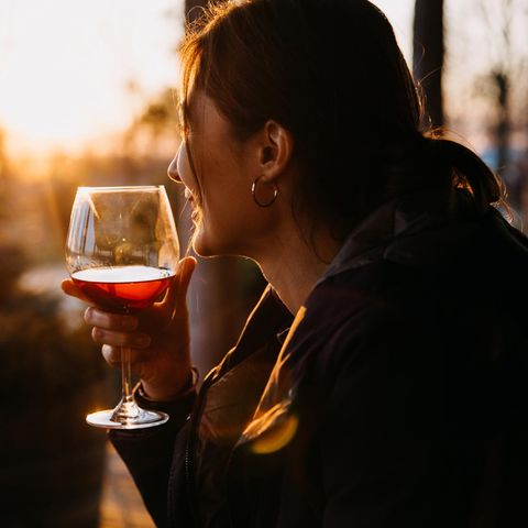 Eine Frau trinkt ein Glas Rotwein, während draußen die Sonne untergeht.
