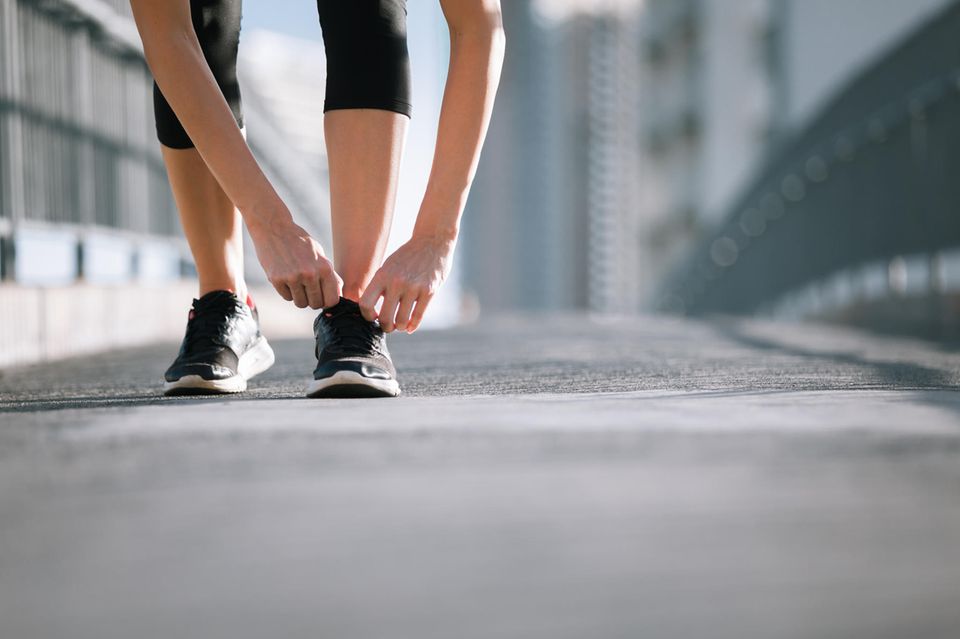 Frau bindet Sportschuhe: Mit diesen 5 Fitness-Hacks wird Ihr Spaziergang zum Workout