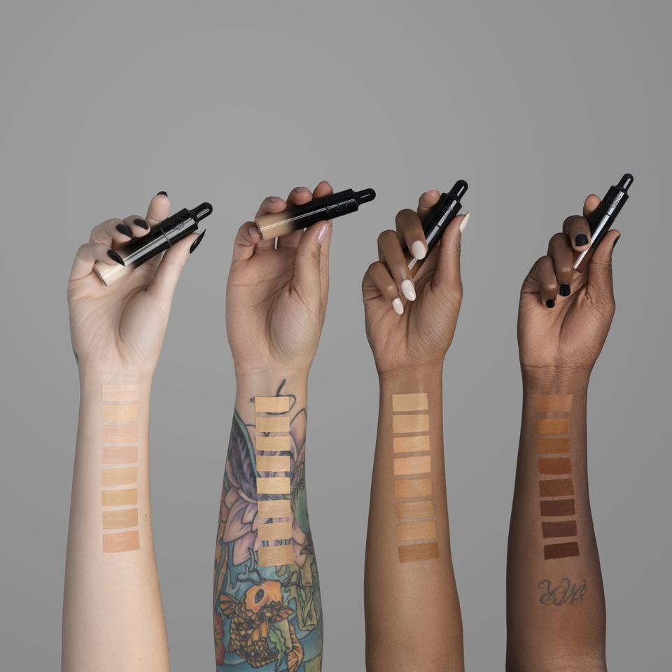 Vier Hände halten den Good Apple Concealer von KVD Beauty hoch.