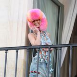 Huch, was ist das denn für eine schräge Kombination? Bella Hadid ist gerade anlässlich der Fashion Week in Paris. Die 25-Jährige präsentiert sich auf einem Pariser Balkon in einem schrillen XL-Fellhut und kombiniert dazu ein rosafarbiges Bralette und eine auffällige Logo-Kette von Louis Vuitton. Die helle Jeans mit roten Stickereien vollendet den ausgefallenen Look.
