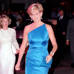 Ihre Schwiegermutter wusste schon vor 26 Jahren, wie edel Azurblau in Kombination mit einem One-Shoulder-Schnitt und großen Ohrringen aussehen kann. Bei ihrer ersten Solo-Reise nach Australien im Jahr 1996 trägt Lady Diana ein Kleid mit asymmetrischer Schulterpartie, das glatt als minimalistischer Zwilling von Meghans Tunika-Kleid durchgehen könnte. Die Robe aus blauem Satin trägt die Handschrift einer ihrer damaligen Lieblingsdesigner, Versace, und wirkt aufgrund seiner klaren Schnitte unaufdringlich und schick. Eine wahre Inspiration eben!
