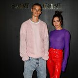 Victoria Beckham erscheint bei der Show von Saint Laurent in Begleitung ihres Sohnes Romeo. In ihrer knalligen Kombi aus Latexhose in Rot und Strickpullover in Lila– natürlich aus eigener Feder – fällt die Designerin direkt auf.