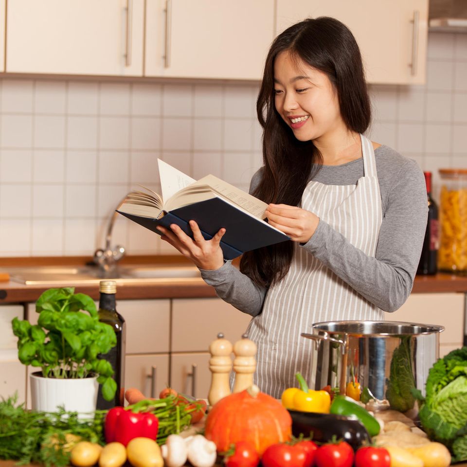 Junge Frau mit Kochbuch und Gemüse in der Küche