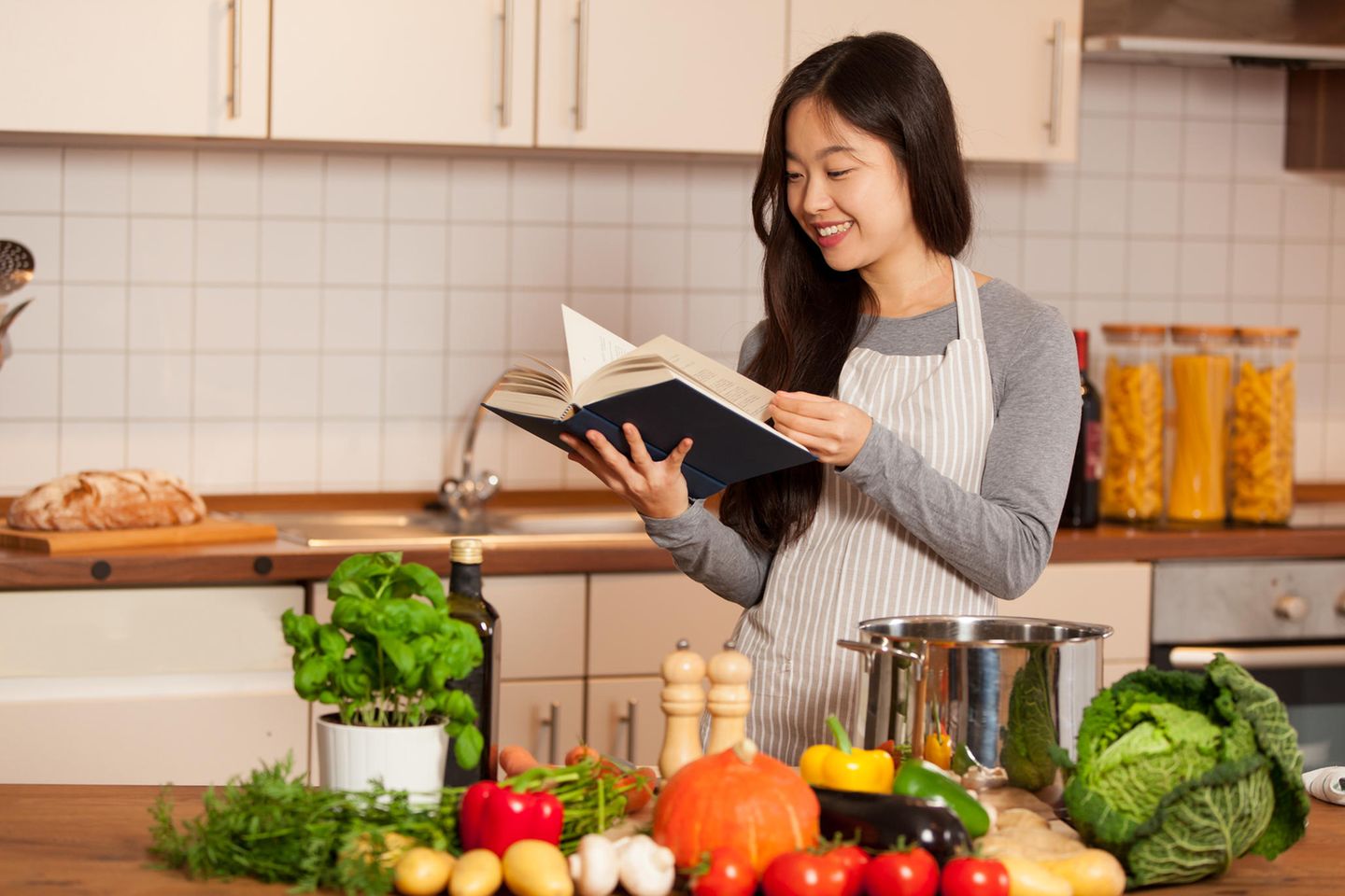 Junge Frau mit Kochbuch und Gemüse in der Küche