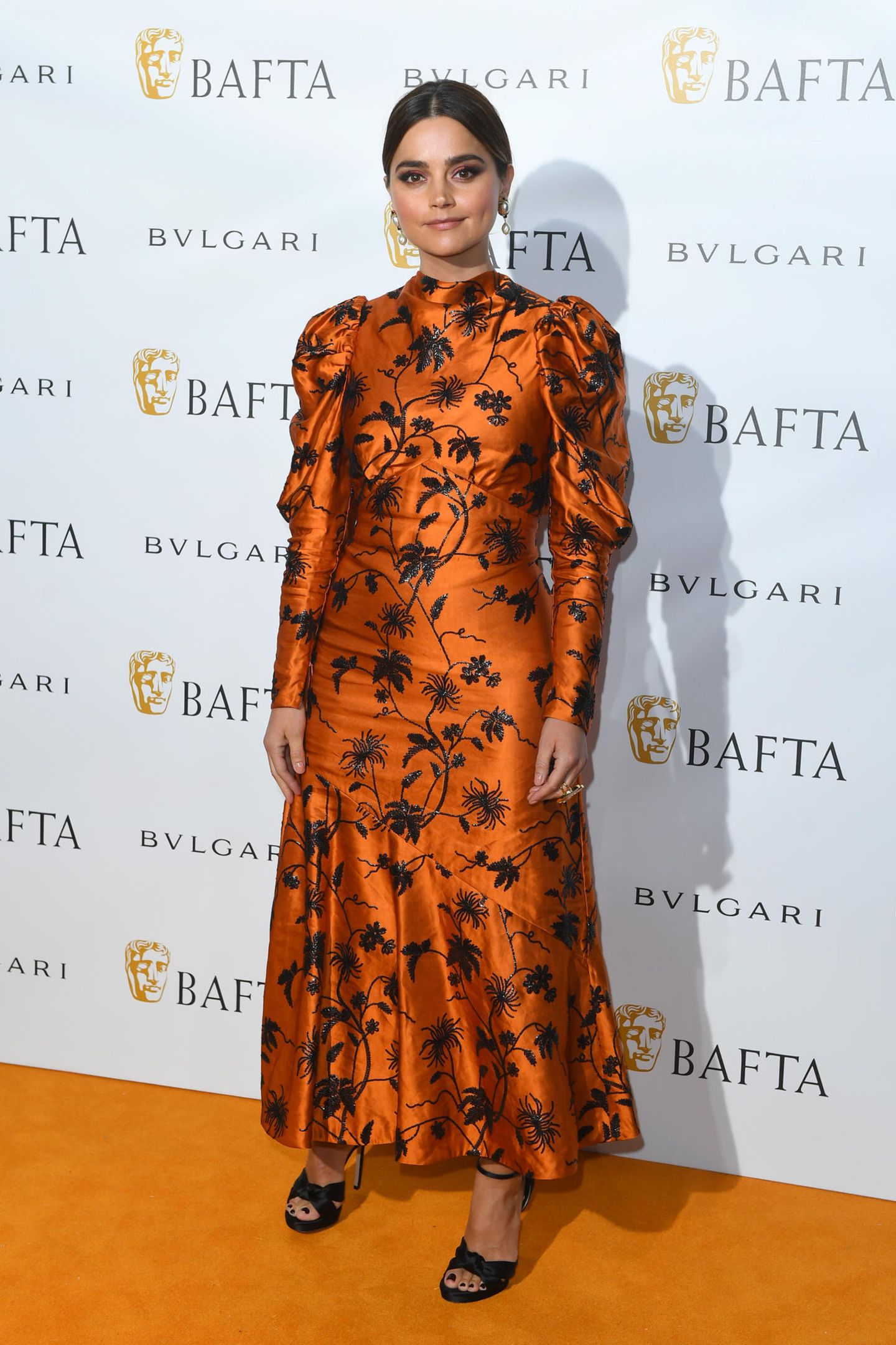 Ob das Zufall ist? Passend zum orangefarbenen Teppich, erscheint auch Schauspielerin Jenna Coleman in einer Robe mit Puffärmeln und Blumen-Muster in Orange. 