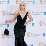 Lady Gaga schreitet in einem smaragdgrünen Kleid mit einer dramatischen Schleppe von Ralph Lauren über den roten Teppich der BAFTAs. Dazu setzt die Schauspielerin auf eine passende Halskette sowie Ohrringe von Tiffany & Co. aus Diamanten und Smaragden. Ihre platinblonden Hollywood-Locken runden den eleganten Diven-Look ab.