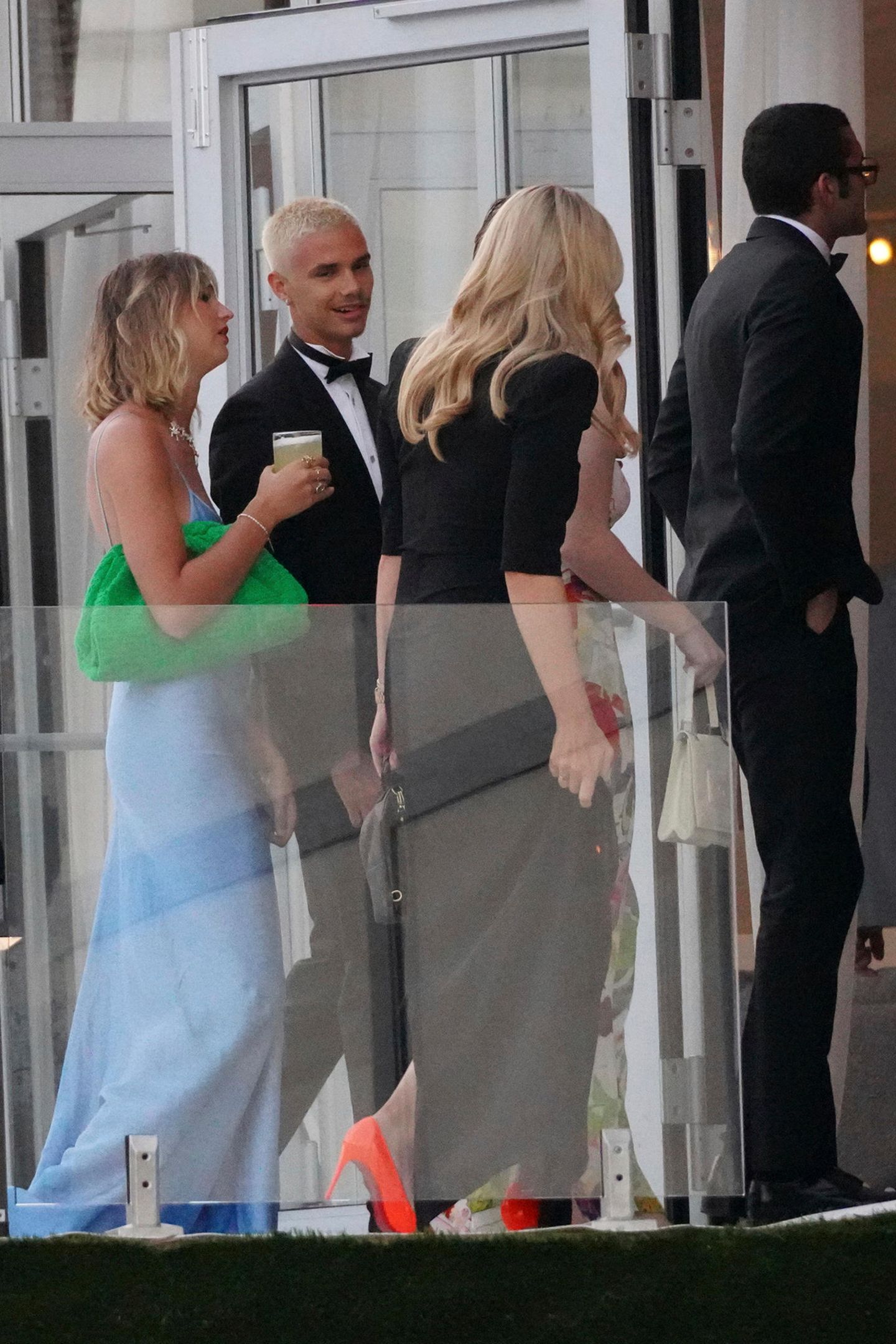 Auch Romeo Beckham setzt auf einen schwarzen, klassischen Anzug in Schwarz mit Fliege. Seine Freundin Mia Regan trägt ein hellblaues Fit-and-Flair-Kleid. Dazu kombiniert das Model eine grüne Clutch.