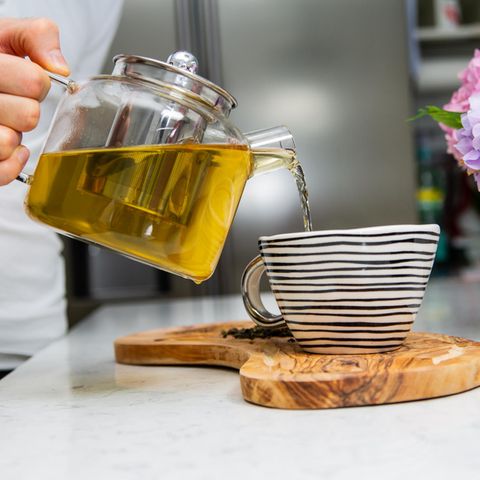 Mann schüttet Tee aus Teekocher in Porzellanbecher, Teekanne