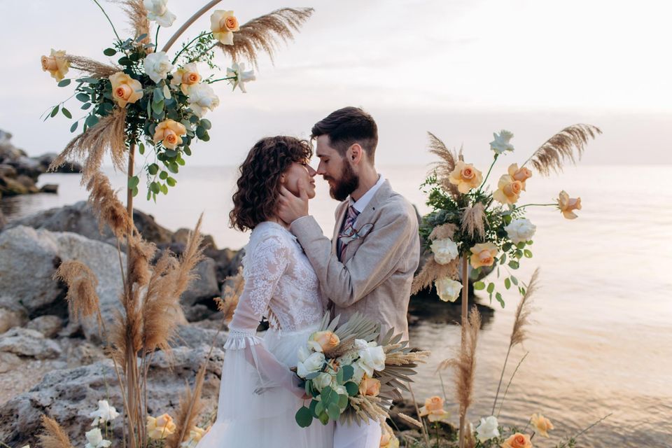 Mann und Frau küssen sich auf ihrer Boho-Hochzeit am Meer