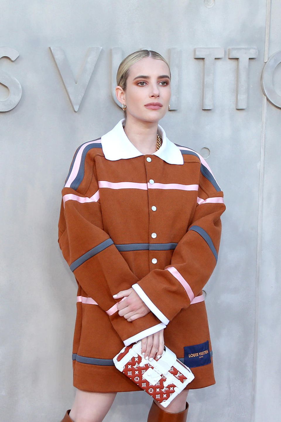 Emma Roberts erschien in einem cognacfarbenen Kurzmantel mit weißem Kragen und Streifen. Die Haare hatte sie in einem strengen Mittescheitel gestylt, toppt ihren Look mit einer kleine Koffer-Tasche des Labels.