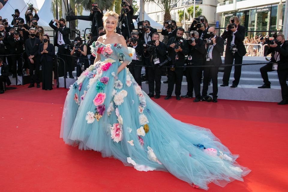 Sharon Stone besucht die Filmfestspiele Cannes 2021 in einer hellblauen Tüllrobe mit großen Blumenapplikationen von Dolce & Gabbana – ein divenhafter Auftritt wie er im Buche steht.