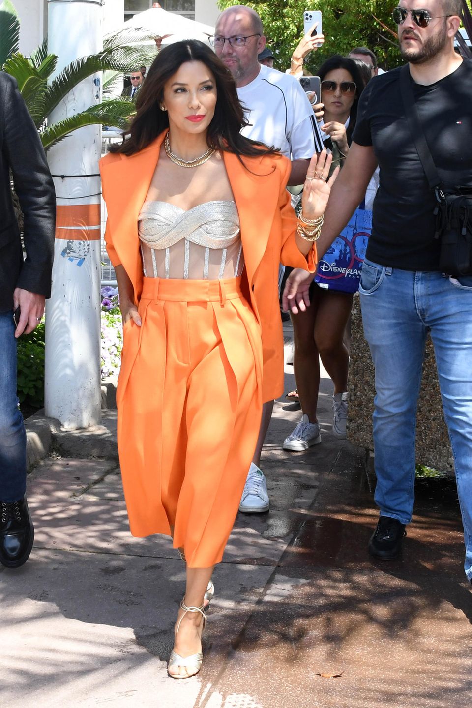 In einem Statement-Suit ist Eva Longoria in den Straßen von Cannes unterwegs. Der Anzug hat breite Schultern, eine extra weite Hose und strahlt in der Trendfarbe Orange. Darunter trägt sie einen Korsett-Artigen Body und goldenen Schmuck.
