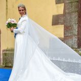 Für die Hochzeit mit ihrem Benedikt wählt Prinzessin Amelie zu Löwenstein-Wertheim-Freudenberg ein weißes Brautkleid mit XL-Schleppe. Dazu trägt sie ein edles Diadem mit Smaragden und einen Brautstrauß aus rosafarbenenen Pfingstrosen und weißen Rosen.