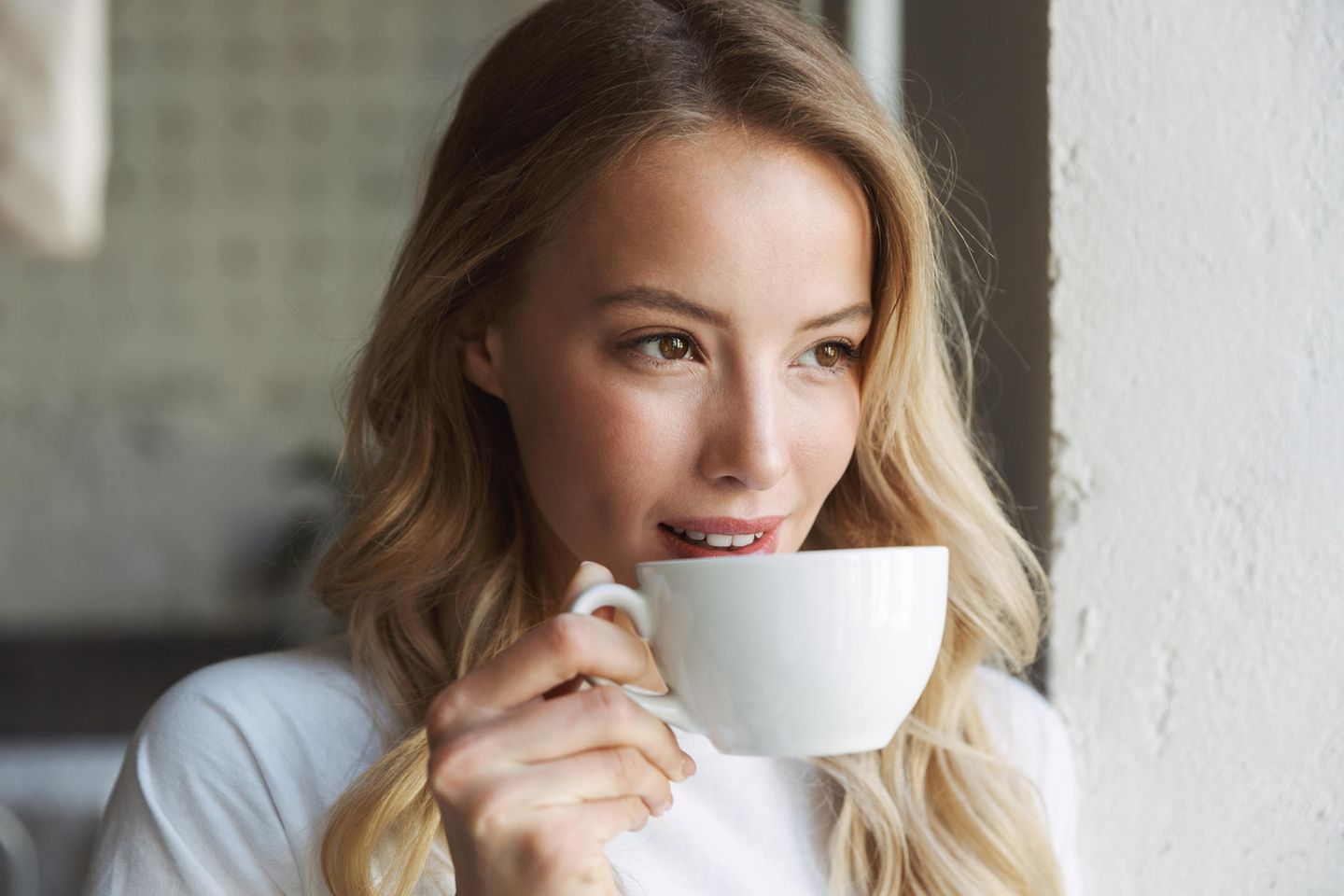 Eine blonde Frau trinkt aus einer Cappuccino-Tasse