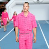 Bei der Marine Serre Menswear Spring Summer 2023 Fashion Show prägten einige interessante und außergewöhnliche Looks den Laufsteg – wie zum Beispiel dieser pinke Look. Das Model trägt ein passendes Set aus einer pink-gemusterten Hose und einem Hemd. Dazu trägt er eine silberne Kette um die Hüfte. 