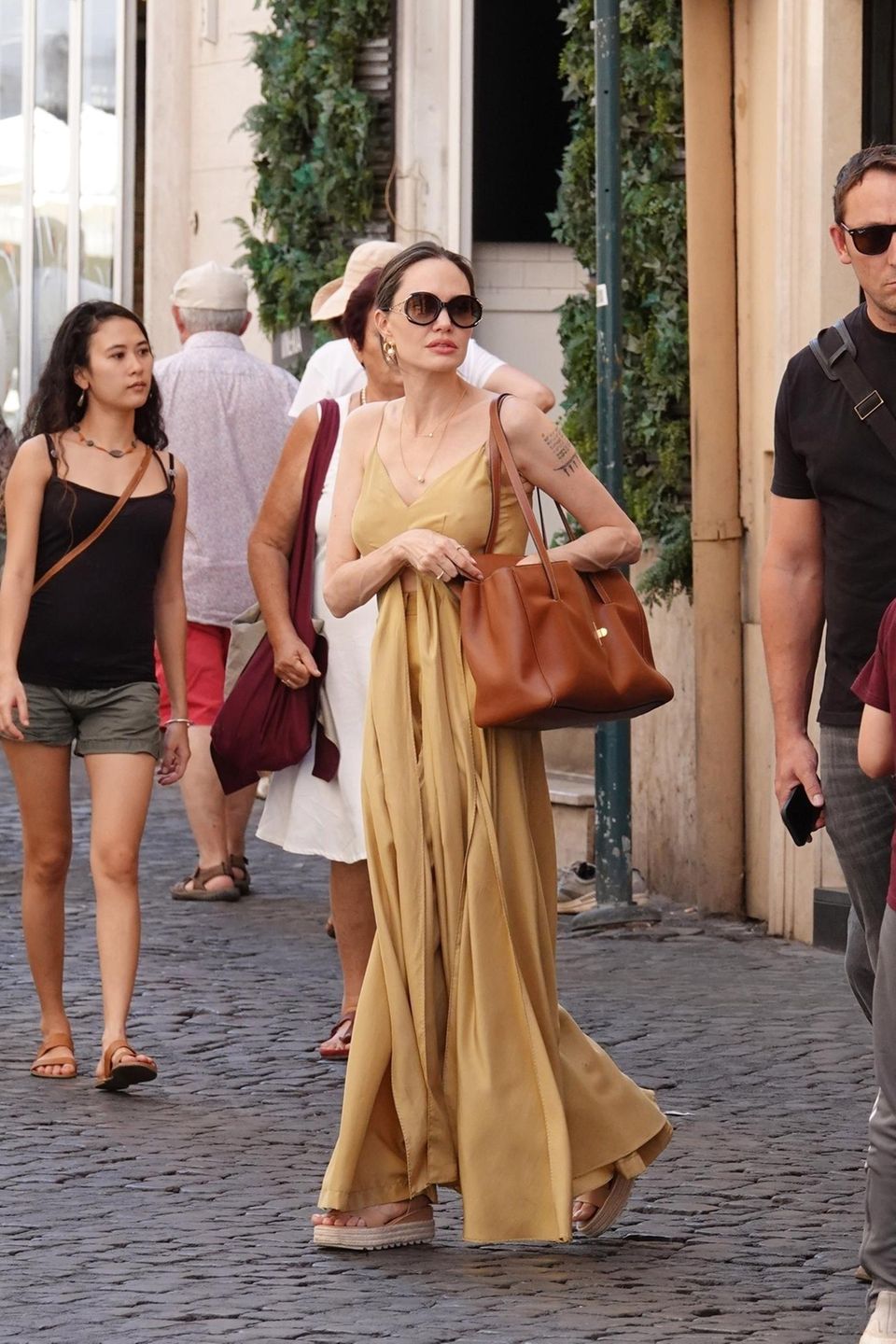 Angelina Jolie verbringt gerade ein paar Tage mit ihren Kindern in Rom – inklusive Shoppingtrip. Auf den ersten Blick scheint sie auf ein senffarbenes Maxikleid zu setzen. Doch wer das Outfit genauer unter die Lupe nimmt, dem fällt eine Sache auf: Bei ihrem Outfit handelt es sich gar nicht um ein Kleid. Angelina setzt auf eine Hose und ein farblich passendes Top mit bodenlangen Details, die an ein Kleid erinnern. Ein raffinierter Trick, der Glamour und Komfort verbindet.
