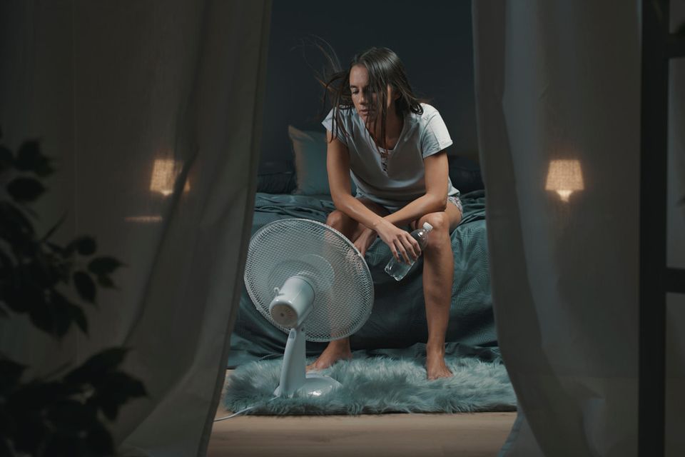 Frau sitzt nachts auf Bettkante vor Ventilator
