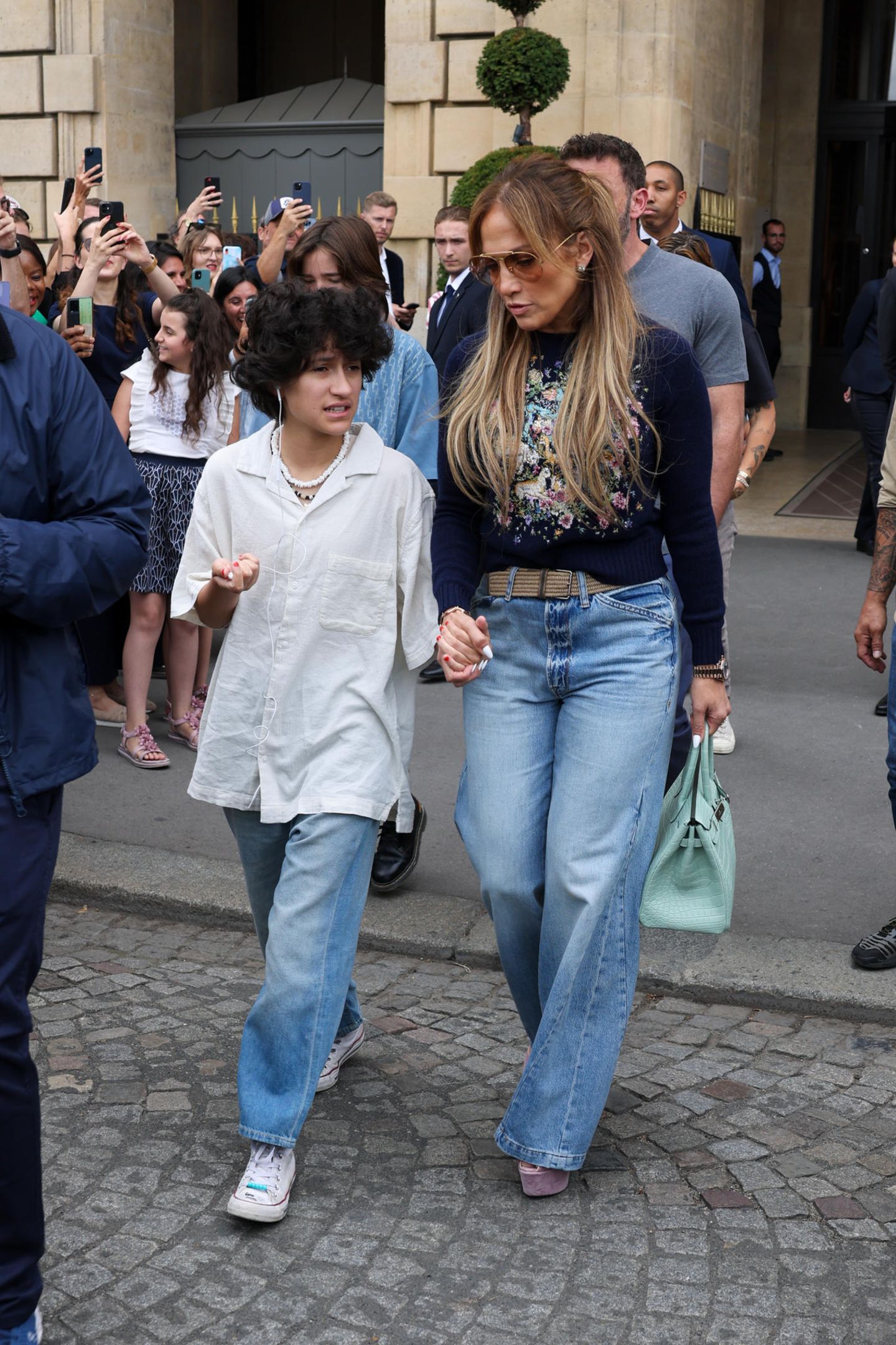 Beim erneuten Auftritt mit Mama Jennifer Lopez – während der Flitterwochen mit ihrem frischgebackenen Ehemann Ben Affleck in Paris Ende Juli 2022 – hat Emme den weißen XXL-Pullover gegen ein lässiges Hemd eingetauscht. Die ebenfalls weiße Korallenkette verleiht dem Look einen 90er-Jahre-Vibe. Auch hier kann der Teenager nicht auf seine blaue Jeans und Schnür-Sneaker verzichten.