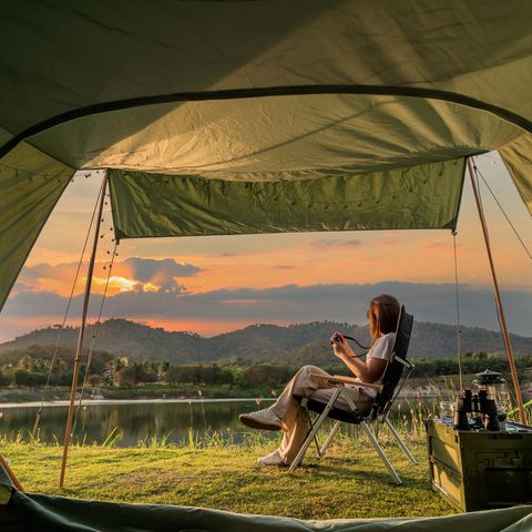 Deals des Tages: Schnell Top-Zelt von High Peak sichern und 30 Euro sparen, entspannte Frau mit Kaffee vor Zelt, Sonnenaufgang