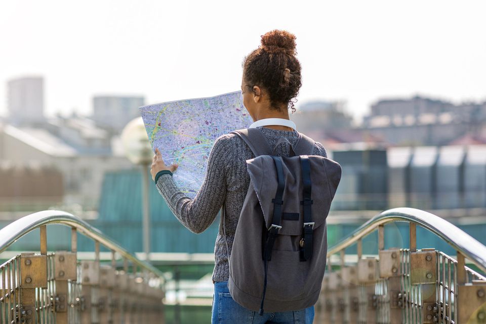 Frau mit Landkarte auf einer Brücke: Reisen macht nicht nur glücklich, sondern auch klüger