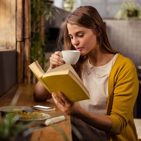 Frau liest ein Buch neben ihrem Smartphone: Diese 7 Trendbücher sind zu Recht Bookstagram-Hypes