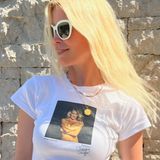 Es ist ein Foto, auf dem Claudia Schiffer nackt ist. Die Arme verschränkt sie vor der Brust. Das Shirt stammt aus ihrer Kooperation mit dem Label Réalisation Par und kostet ca. 80 Euro. 