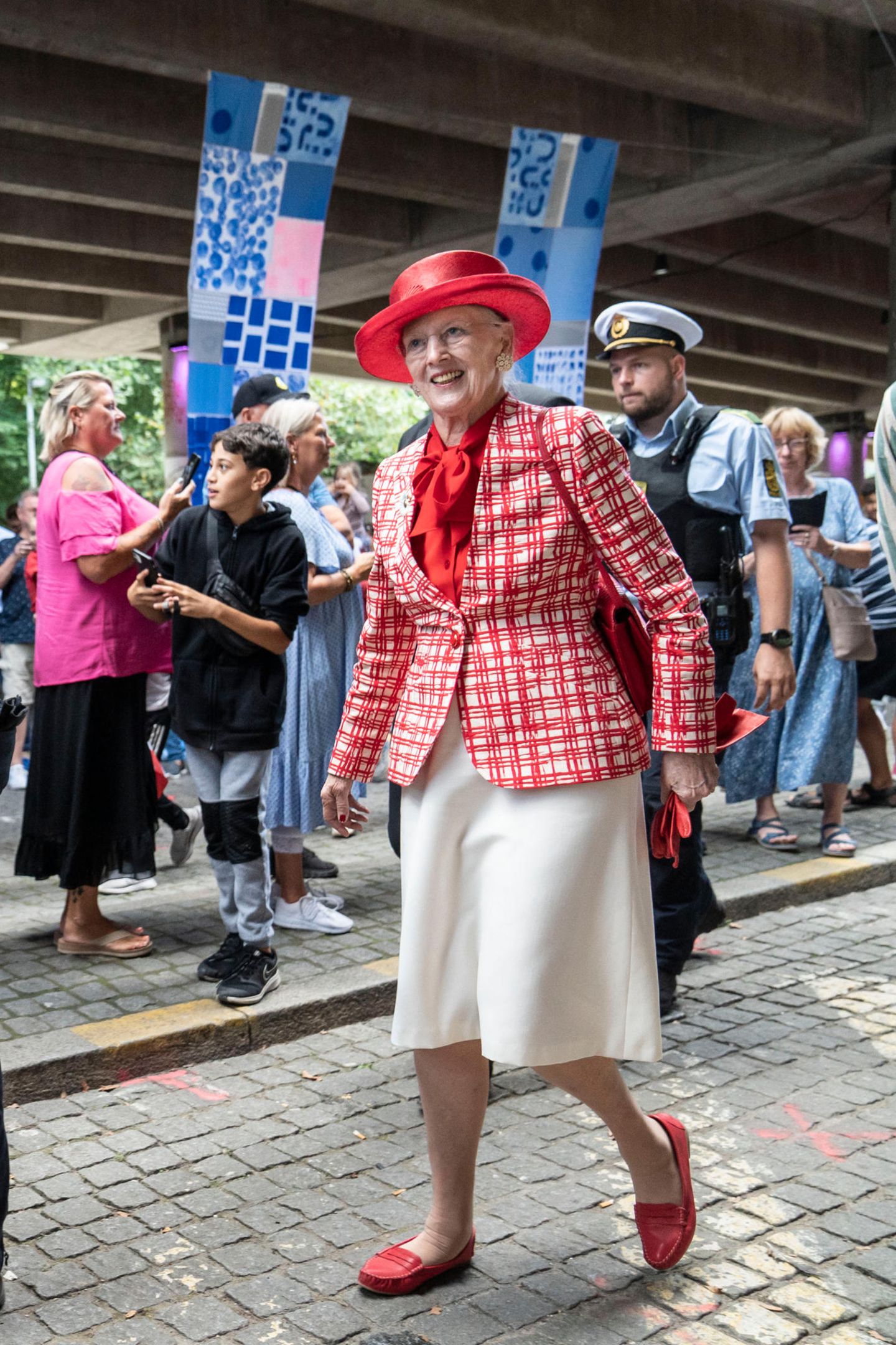 Beim Besuch der Kommune Frederiksberg mit der Königsyacht Dannebrog zeigt sich Königin Margrethe in den Farben ihres Landes. Zum weißen Rock kombiniert sie ein weiß-rot-kariertes Jackett. Auch die Accessoires sind rot, Schuhe, Einstecktuch und Hut erstrahlen in dem kräftigen Farbton.