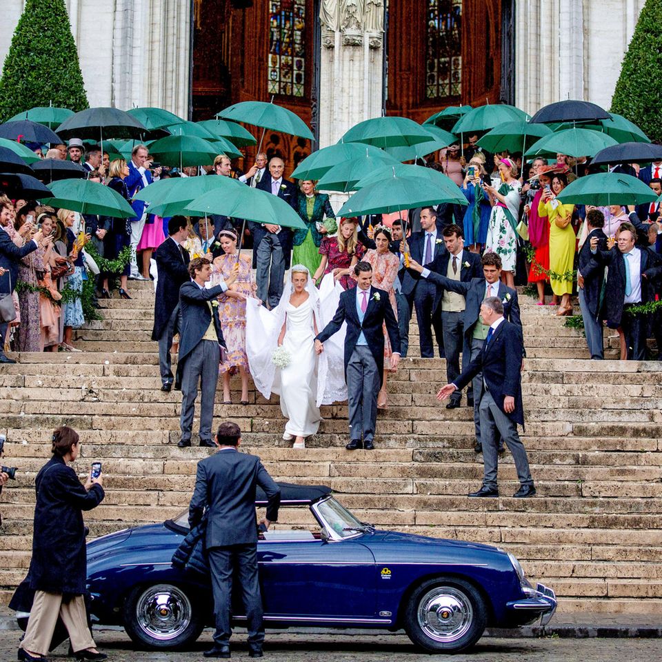 Jetzt kann gefeiert werden: Das Brautpaar, geschützt von den vielen Regenschirmen, verlässt die Kathedral in einem Porsche-Oldtimer Richtung Hochzeitsfeier.