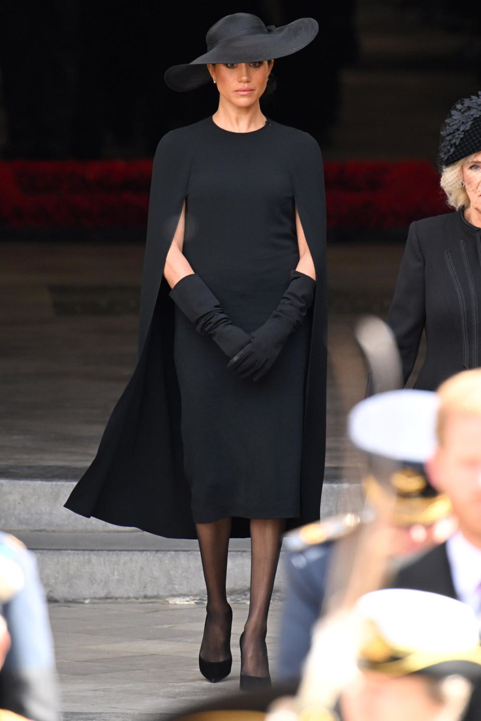 Herzogin Meghan trifft bei der Beerdigung von Queen Elizabeth ein. Die Frau von Prinz Harry trägt ein Cape-Dress von Stella McCartney in Midilänge, dazu eine schwarze Strumpfhose sowie einen schwarzen Hut von Dior. Um ihre Arme zu bedecken, greift Meghan in der Kirche zu langen schwarzen Handschuhen.