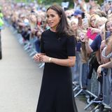 Zwei Tage nach dem Tod von Queen Elizabeth besucht Herzogin Meghan mit Prinz Harry, Prinz William und Catherine, Princess of Wales, Trauernde, die vor den Toren von Windsor Castle warten. Dazu trägt sie ein schwarzes Midikleid aus Strick mit angedeutetem U-Boot-Ausschnitt und kurzen Ärmeln. Der Rock fällt nach unten hin etwas schwingend auf, dazu kombiniert Meghan schwarze Heels von Sarah Flint mit Absatz in Schildplattoptik.