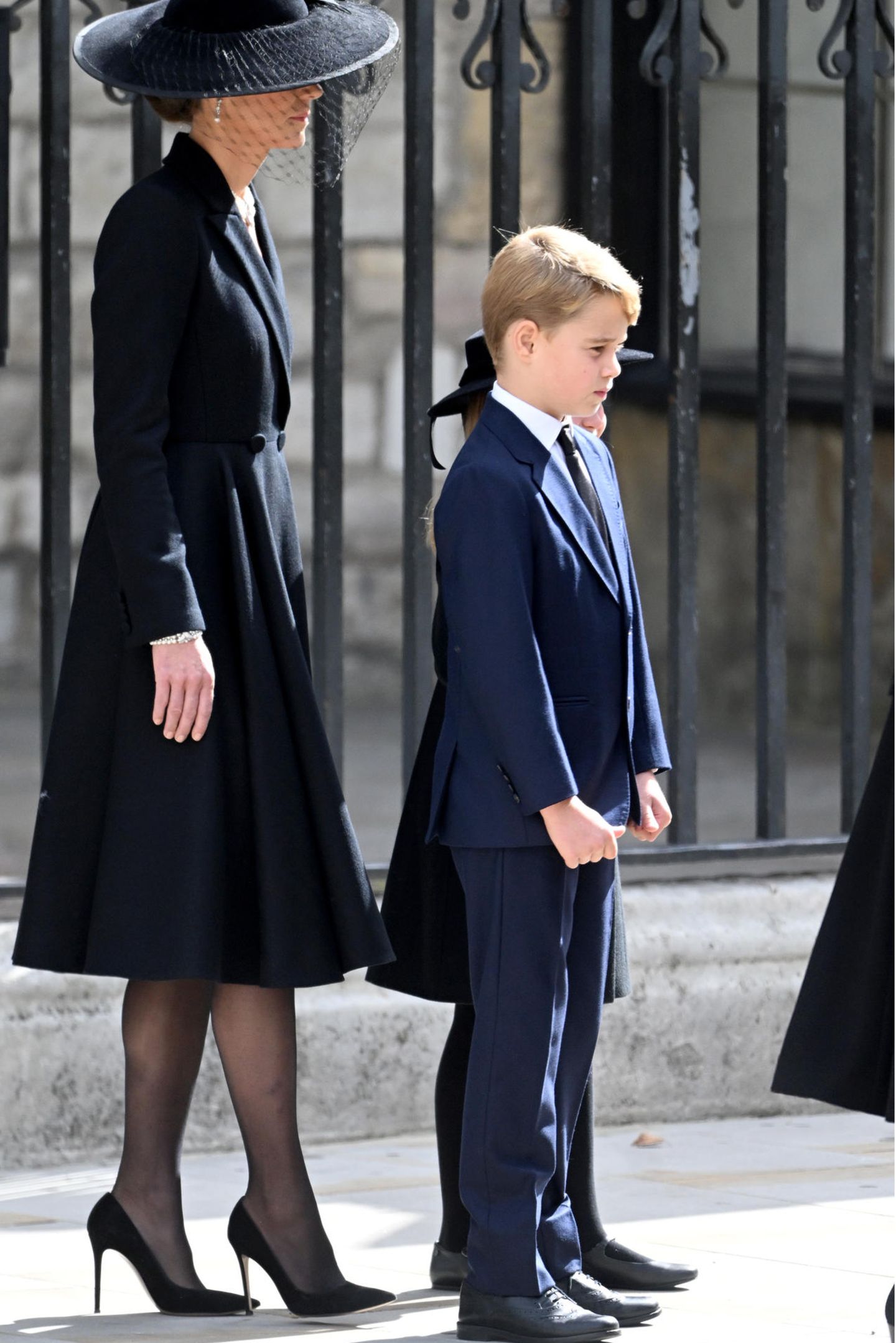 Prinz George erscheint in einem dunkelblauen, nicht in einem schwarzen Anzug. Obwohl Dunkelblau für eine Beerdigung als genau so respektvoll gilt, wie Schwarz, überrascht es. Dazu trägt er ein weißes Hemd und eine schwarze Krawatte. 