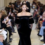 Ein klassischer Frühling-Sommer-Look ist das, was Supermodel Irina Shayk bei der Show von Burberry präsentiert, nicht gerade. Das schwarze Maxikleid mit Carmen-Ausschnitt kommt mit Korsage, Fellbesatz und Spitzenärmeln daher.