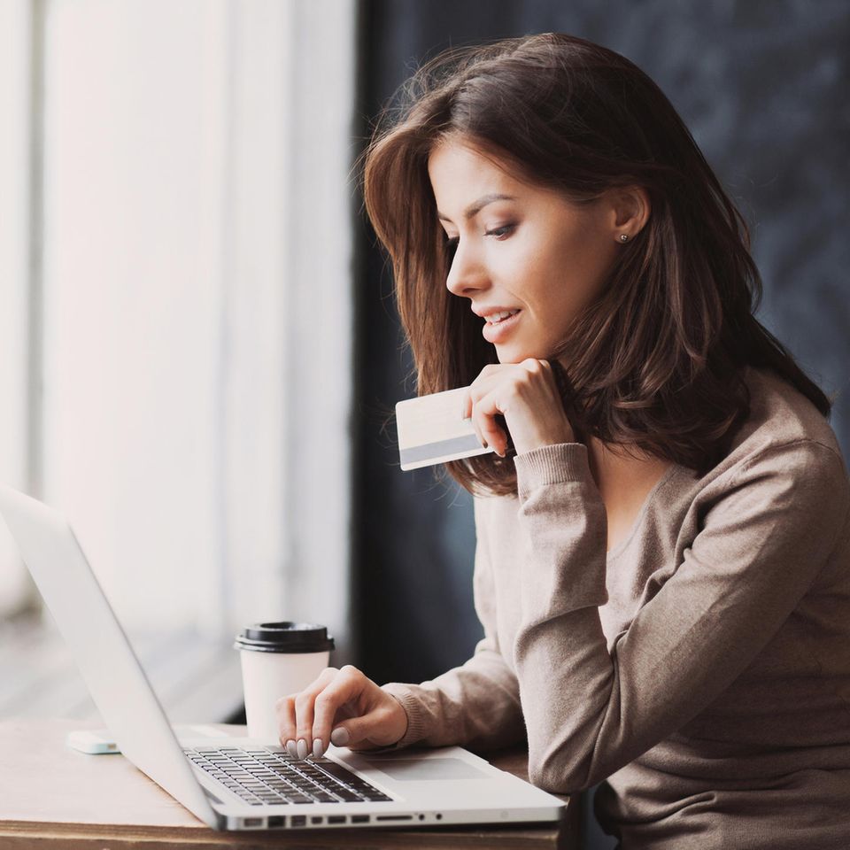 Frau hält Kreditkarte in der Hand und sitzt am Laptop