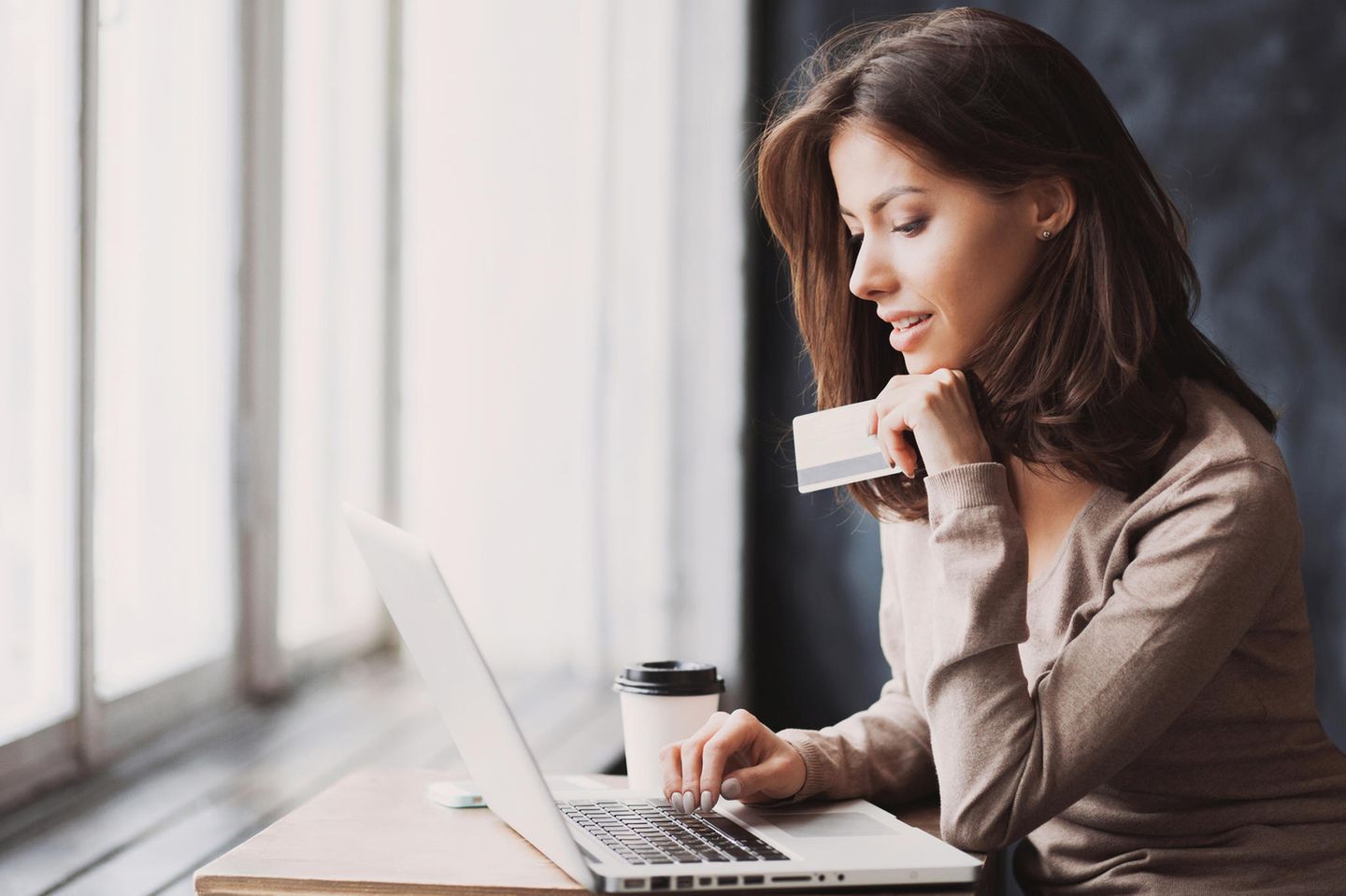 Frau hält Kreditkarte in der Hand und sitzt am Laptop