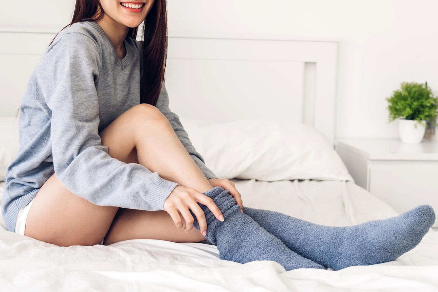Eine junge Frau sitzt auf einem Bett und zieht sich dicke Socken an
