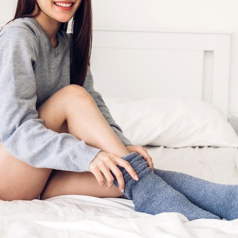 Eine junge Frau sitzt auf einem Bett und zieht sich dicke Socken an